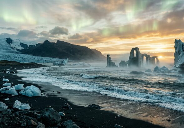 A vast, ethereal arctic landscape at the edge of the known world, where towering glaciers and dark volcanic black sand beaches meet a turbulent iron-grey sea under a midnight sun casting long golden light across the horizon. In the distance, ghostly ruins of ancient stone structures emerge half-submerged from the icy waters, draped in mist. The sky shimmers with faint auroras blending into pale summer light, evoking both timelessness and mystery. The scene feels both majestic and melancholic, as if preserving the memory of a forgotten civilization swallowed by rising seas at the end of the last ice age. Dramatic cinematic lighting, painterly editorial style with rich cool blues, deep teals, and warm amber tones, highly detailed, evocative and atmospheric.